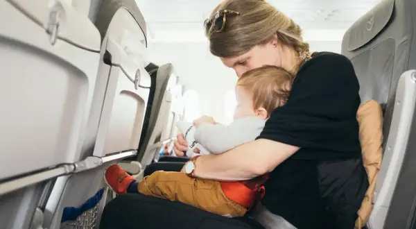 Mama tuli tulot z niemowlakiem w samolocie. Dziecko trzyma zabawkę z logo linii lotniczych.