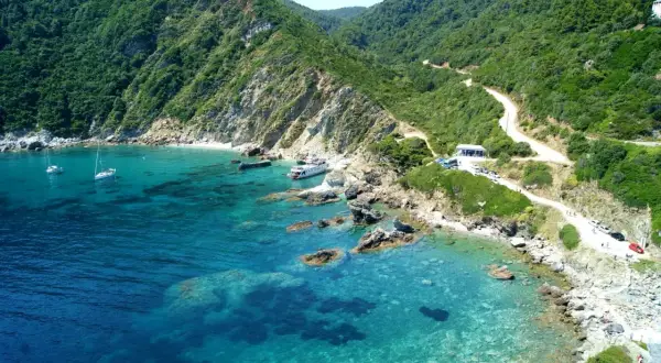 Malownicza zatoka na wyspie Skopelos z krystalicznie czystą wodą, łodziami i krętą drogą wiodącą przez zielone wzgórza.