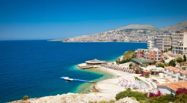 Piękna albania pogoda: błękitne morze, plaża z leżakami i hotelami na wzgórzu.