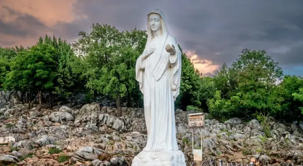 Biały posąg Matki Bożej na skalistym wzgórzu, miejsce pielgrzymek do Medjugorie.