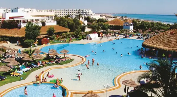 Słoneczny dzień w resorcie, ludzie kąpią się w basenie, a w tle widać morze. To idealne miejsce na wakacje w stylu caribbean world Mahdia.