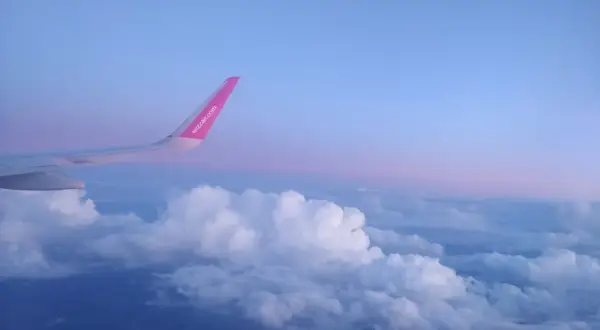 Skrzydło samolotu rejsowego Wizz Air nad chmurami o zachodzie słońca.