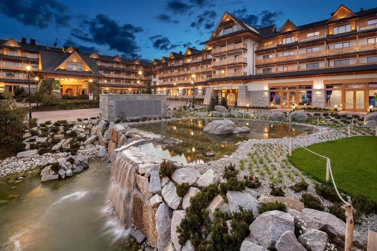 Elegancki hotel z basenami termalnymi, z kaskadą wodną i stawem w otoczeniu kamieni i zieleni.