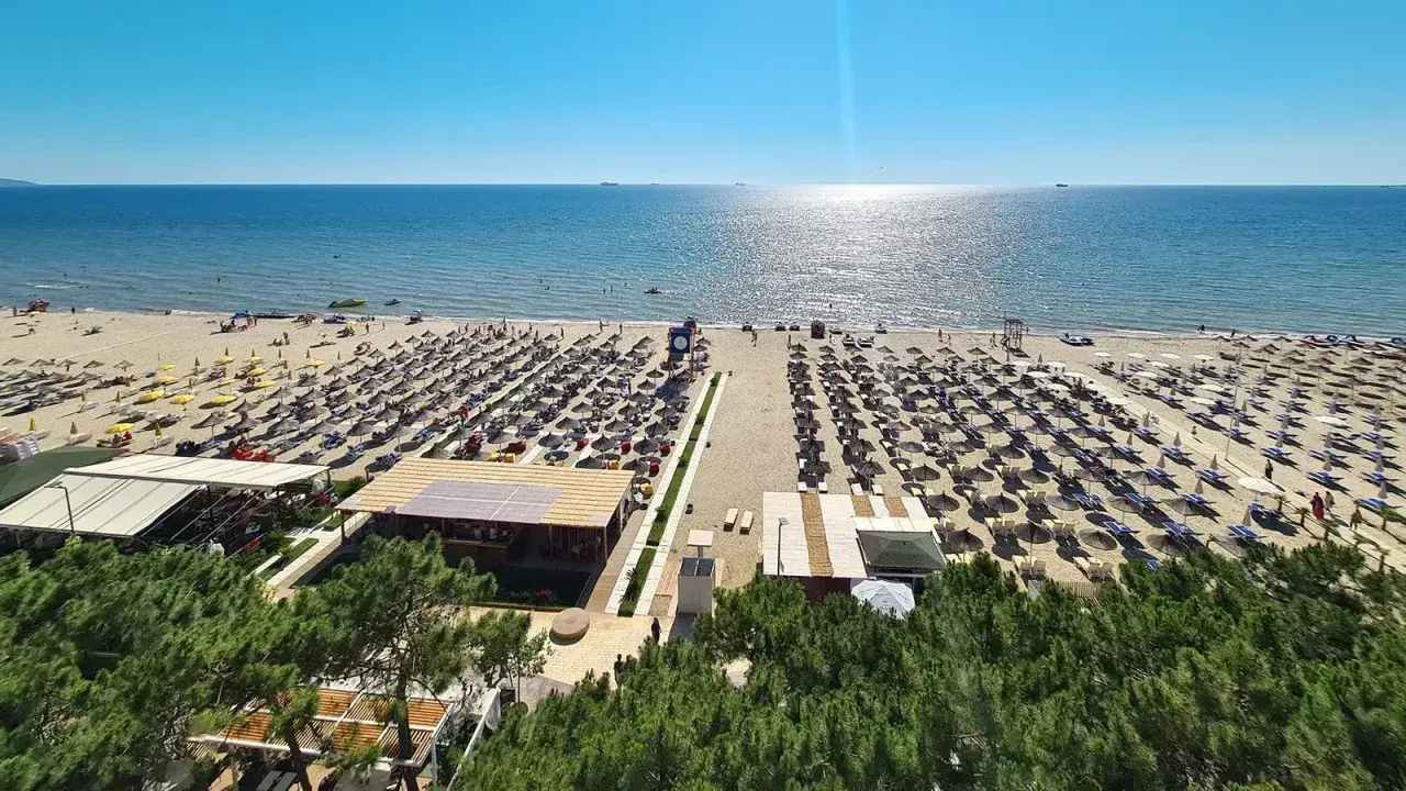 Majowa pogoda w Albanii zachwyca. Słoneczna plaża z rzędami leżaków i parasoli, turkusowe morze i błękitne niebo.