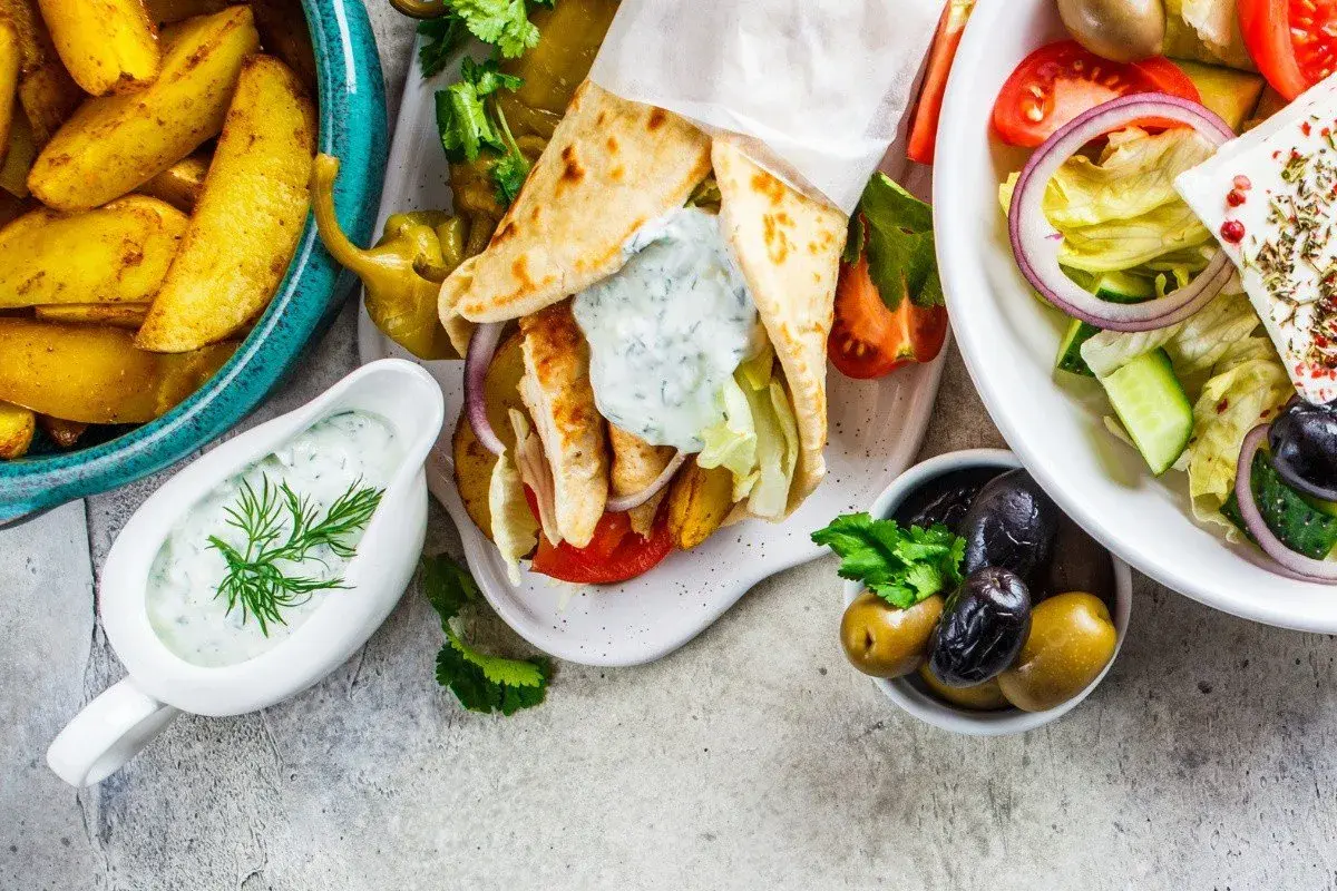 Pyszne dania kuchni greckiej: gyros, sałatka grecka, frytki i sos tzatziki.