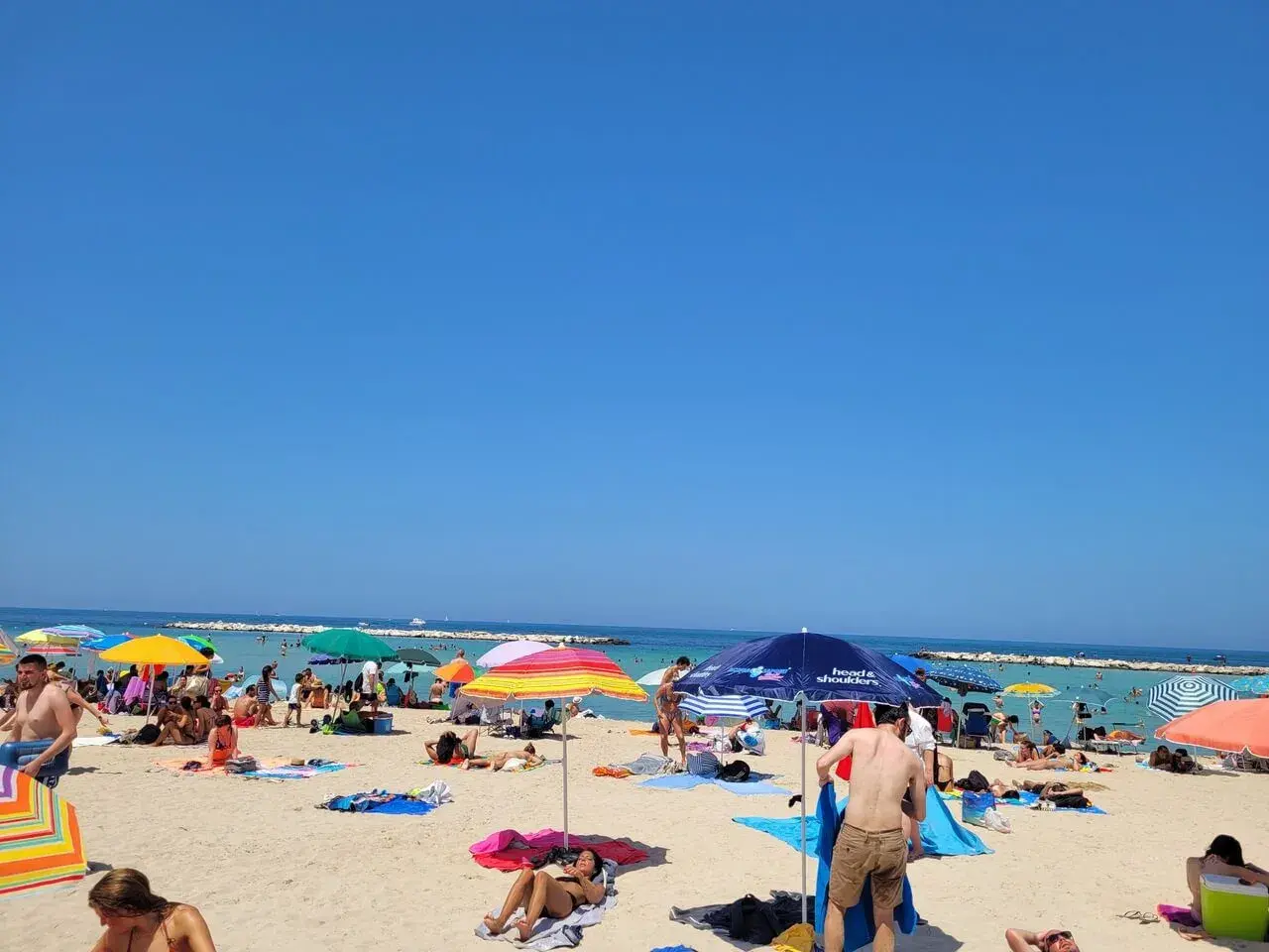 Słoneczne **bari plaże** tętnią życiem. Ludzie opalają się pod kolorowymi parasolami, kąpią w morzu i odpoczywają na piasku.