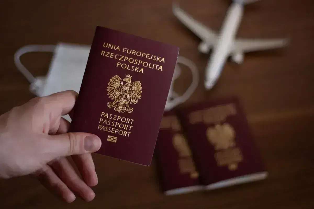 Dłoń trzyma polski paszport. Obok leżą kolejne dokumenty, maseczka i samolot. Zastanawiasz się, ile trwa wyrobienie paszportu?