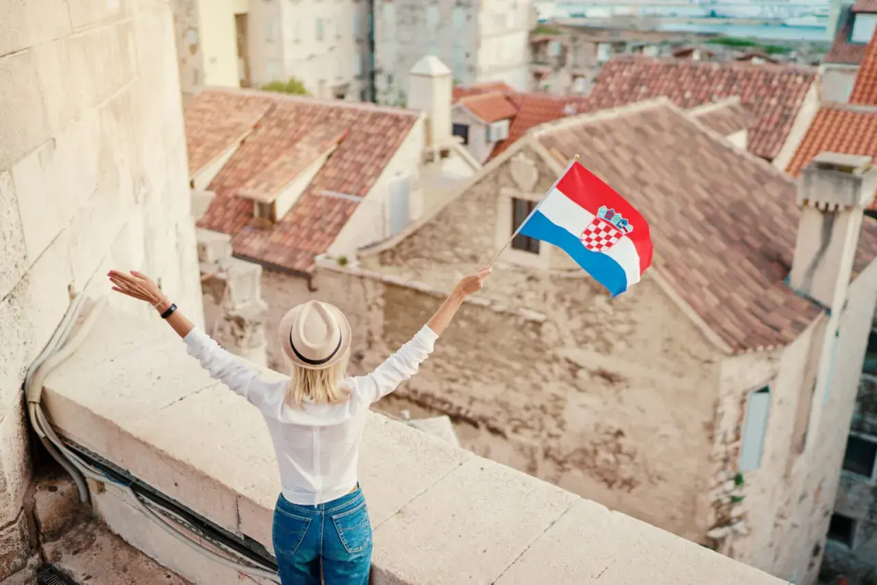 Kobieta z chorwacką flagą na tle dachów. W tle widać piękne, stare miasto.