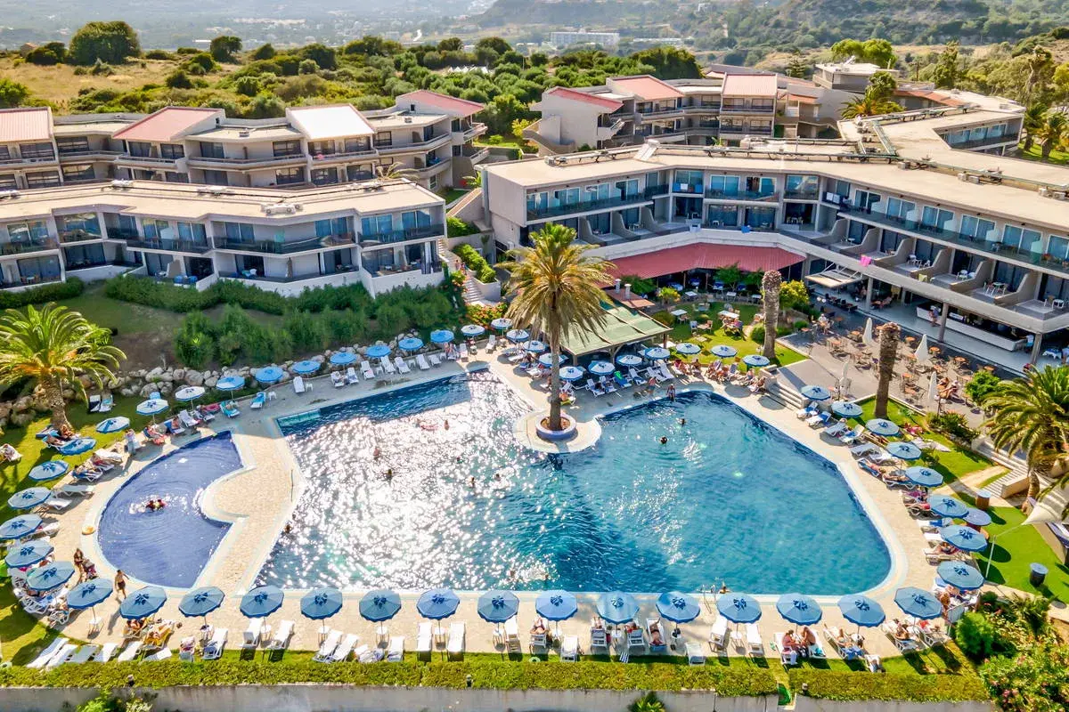 Relaks przy basenie w Cathrin Hotel Rodos. Goście odpoczywają na leżakach pod parasolami, niektórzy pływają w turkusowej wodzie.