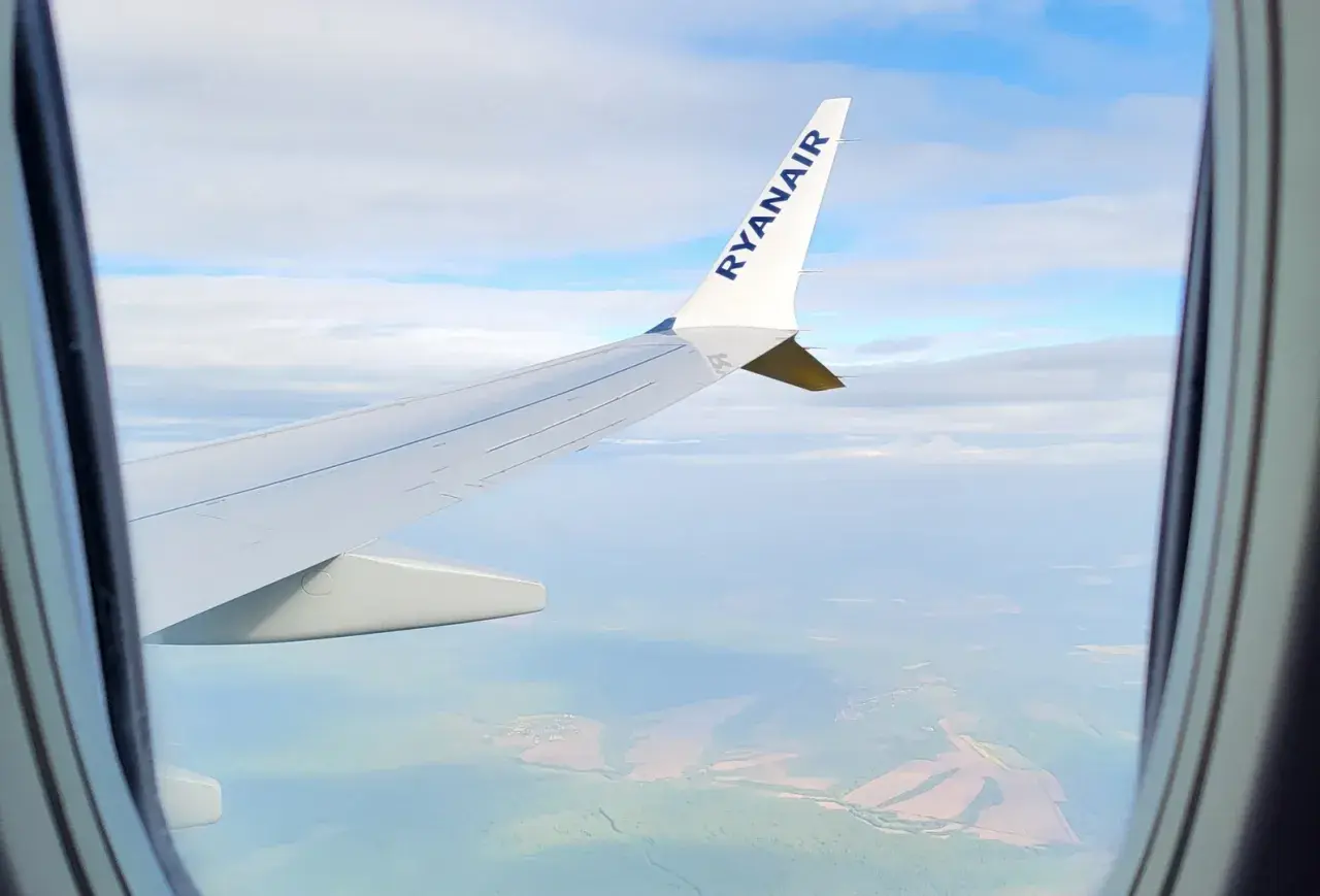 Widok z okna samolotu Ryanair, idealny do nauki, jak szukać tanich wakacji. Podróż nad zielonymi polami i chmurami.