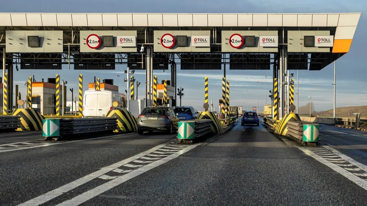 Samochody zbliżają się do bramek poboru opłat za autostrady. Widać znaki eTOLL i ograniczenia wysokości 2,0m.