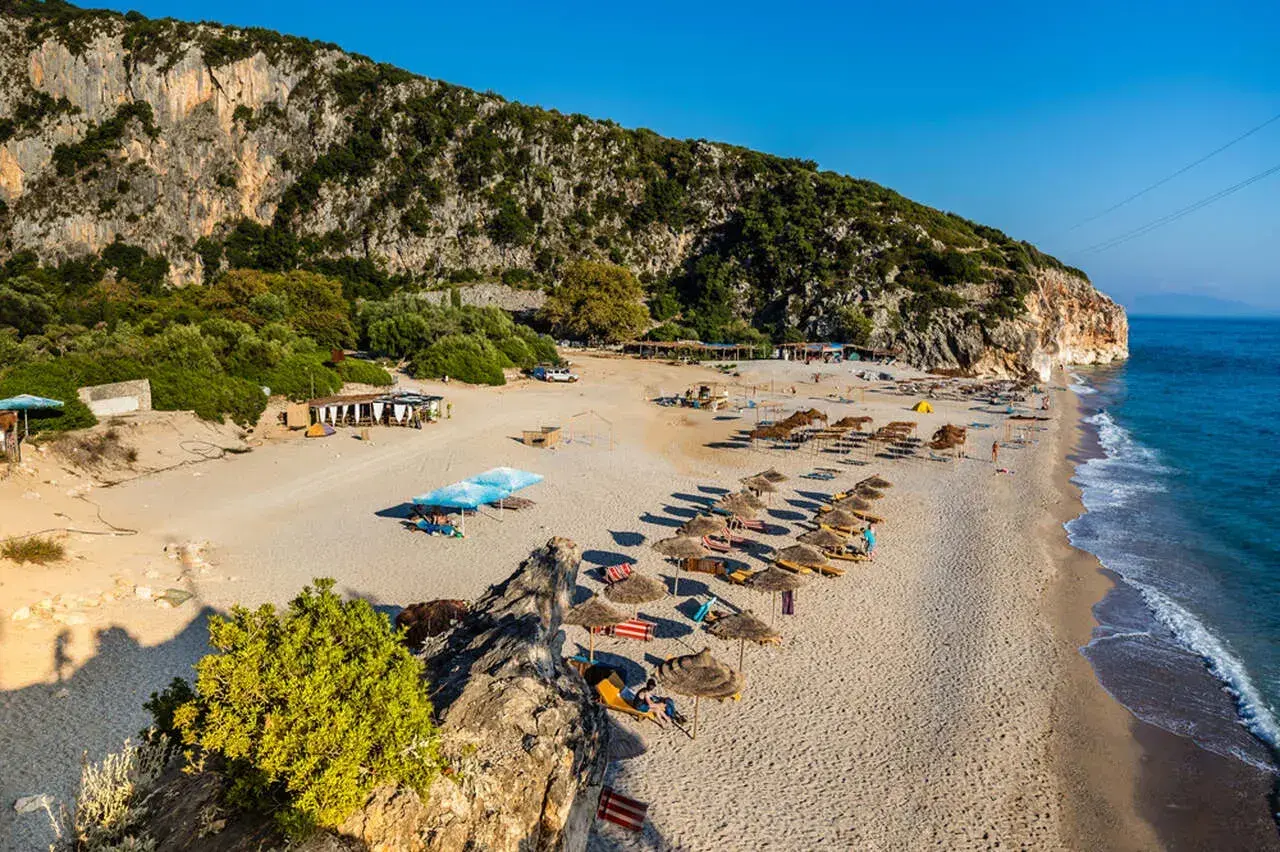 Piękne albania plaże piaszczyste z rzędami parasoli i leżaków, w cieniu skalistego klifu.