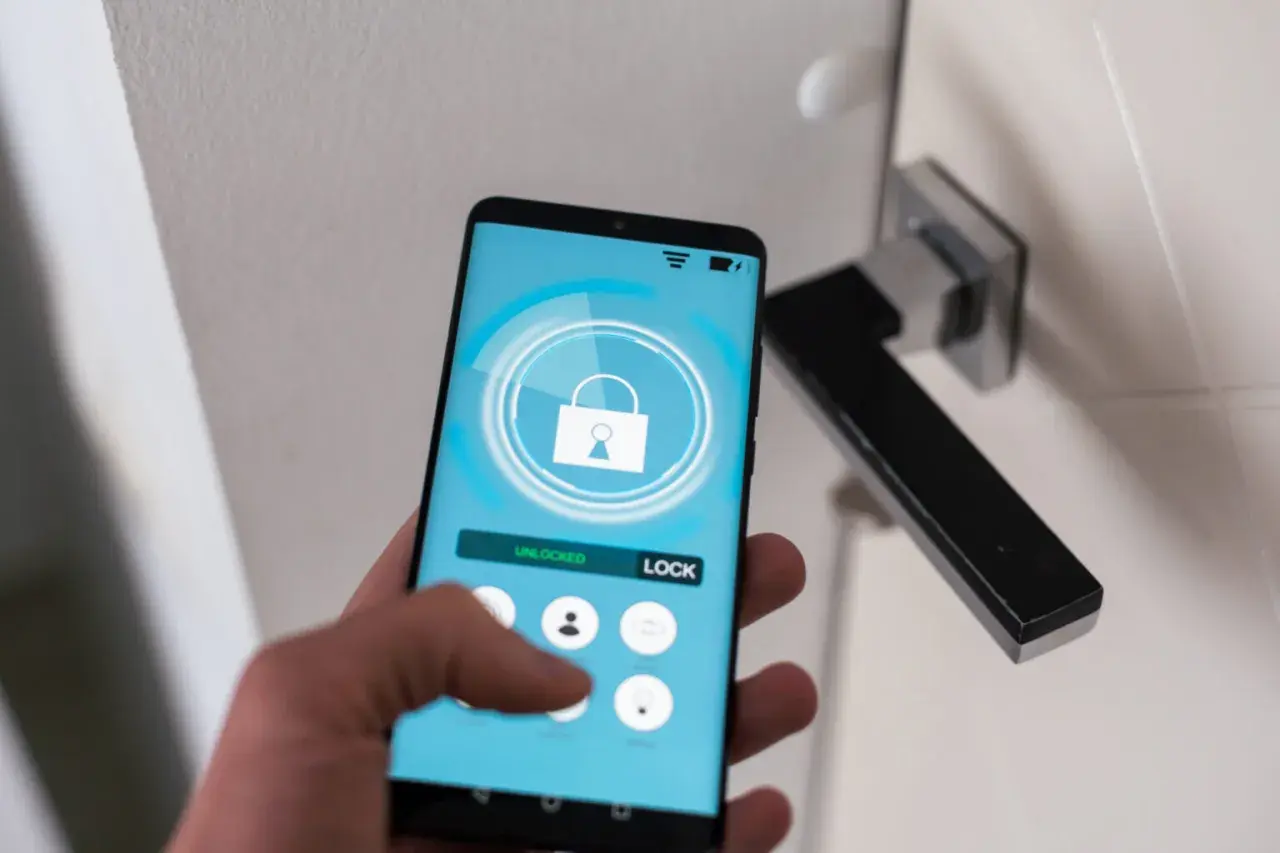 Dłoń trzyma smartfon z aplikacją do zdalnego sterowania zamkiem. Ułatwia to samoobsługowy self check-in.