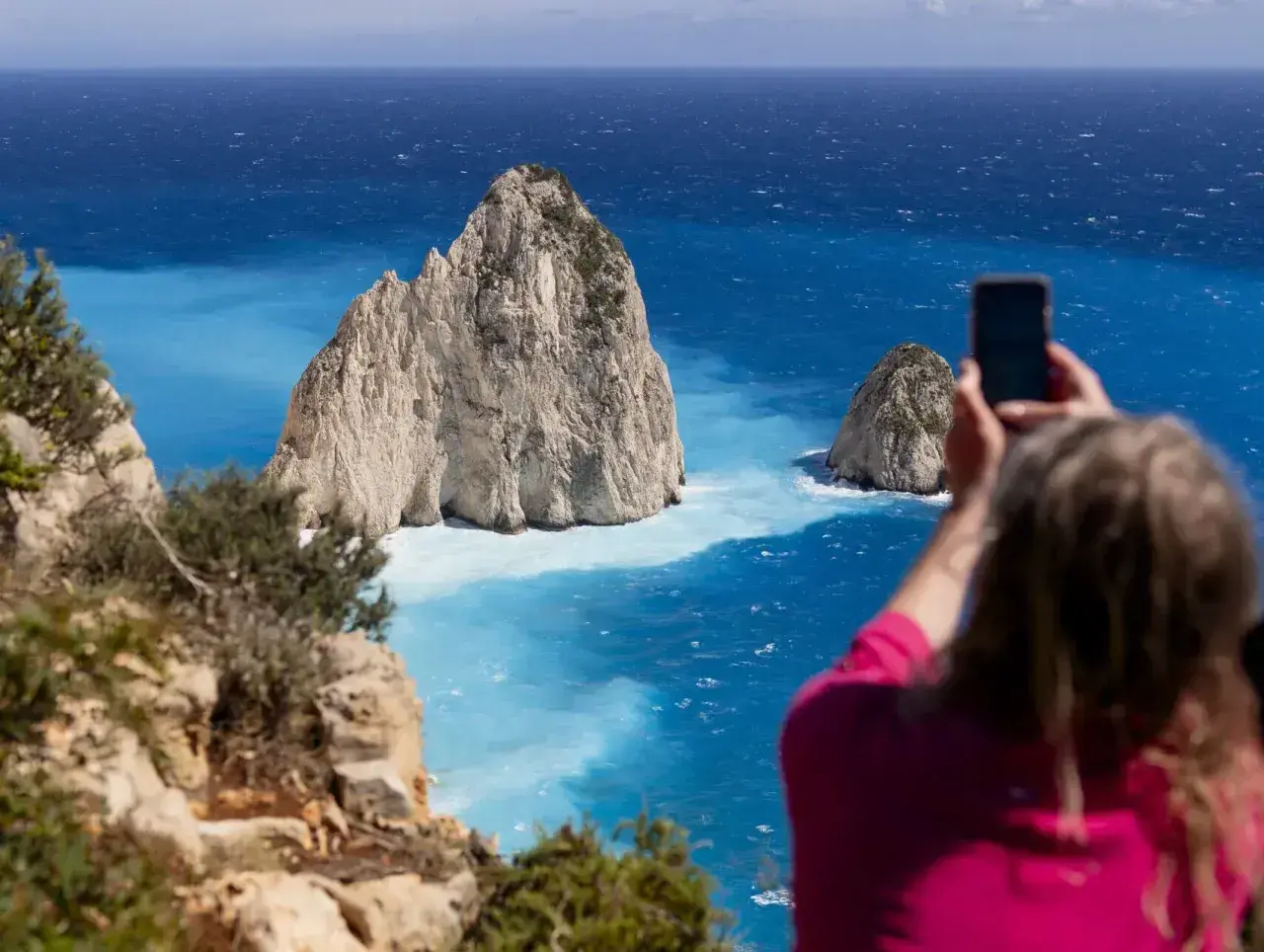Widok na turkusowe morze Zakynthos, gdzie turystka robi zdjęcie skalistym wysepkom.