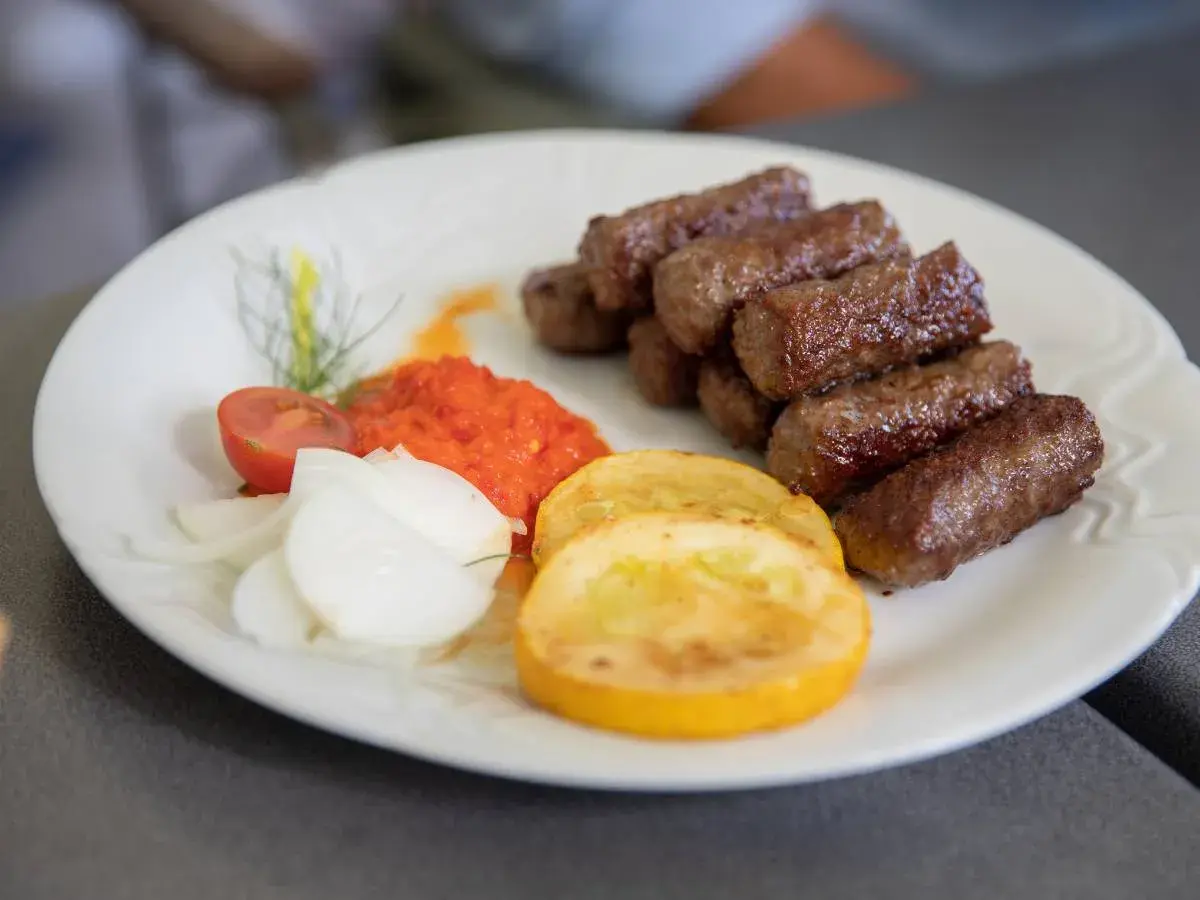 Cevapi, klasyka kuchni słoweńskiej, podane z ajwarem, cebulą i pomidorem.