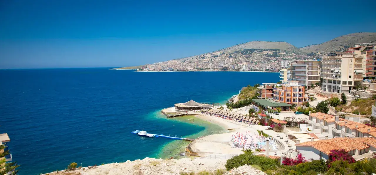Piękna albania pogoda: błękitne morze, plaża z leżakami i hotelami na wzgórzu.
