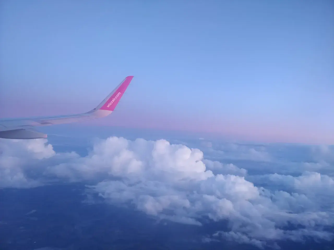 Skrzydło samolotu rejsowego Wizz Air nad chmurami o zachodzie słońca.