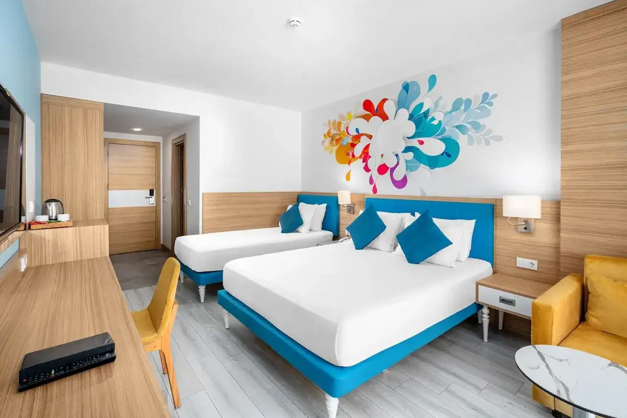 Pokój hotelowy z dwoma łóżkami i kolorową grafiką na ścianie. To jak **club sun heaven** dla podróżnych.