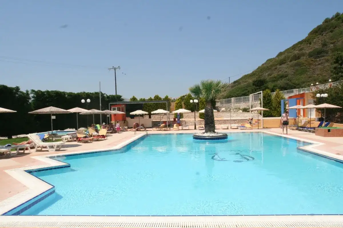 Basen hotelu Diagoras z palmą pośrodku, leżakami i parasolami.