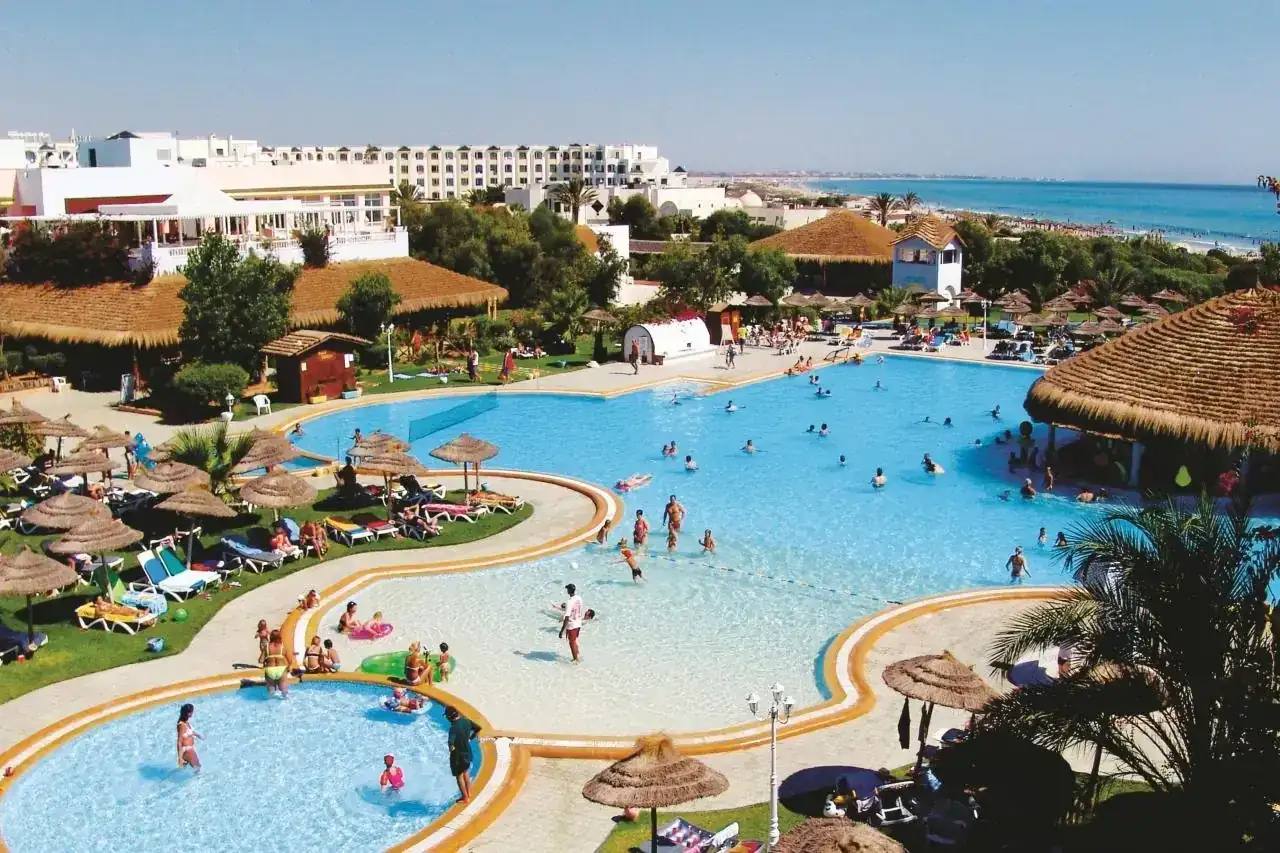 Słoneczny dzień w resorcie, ludzie kąpią się w basenie, a w tle widać morze. To idealne miejsce na wakacje w stylu caribbean world Mahdia.