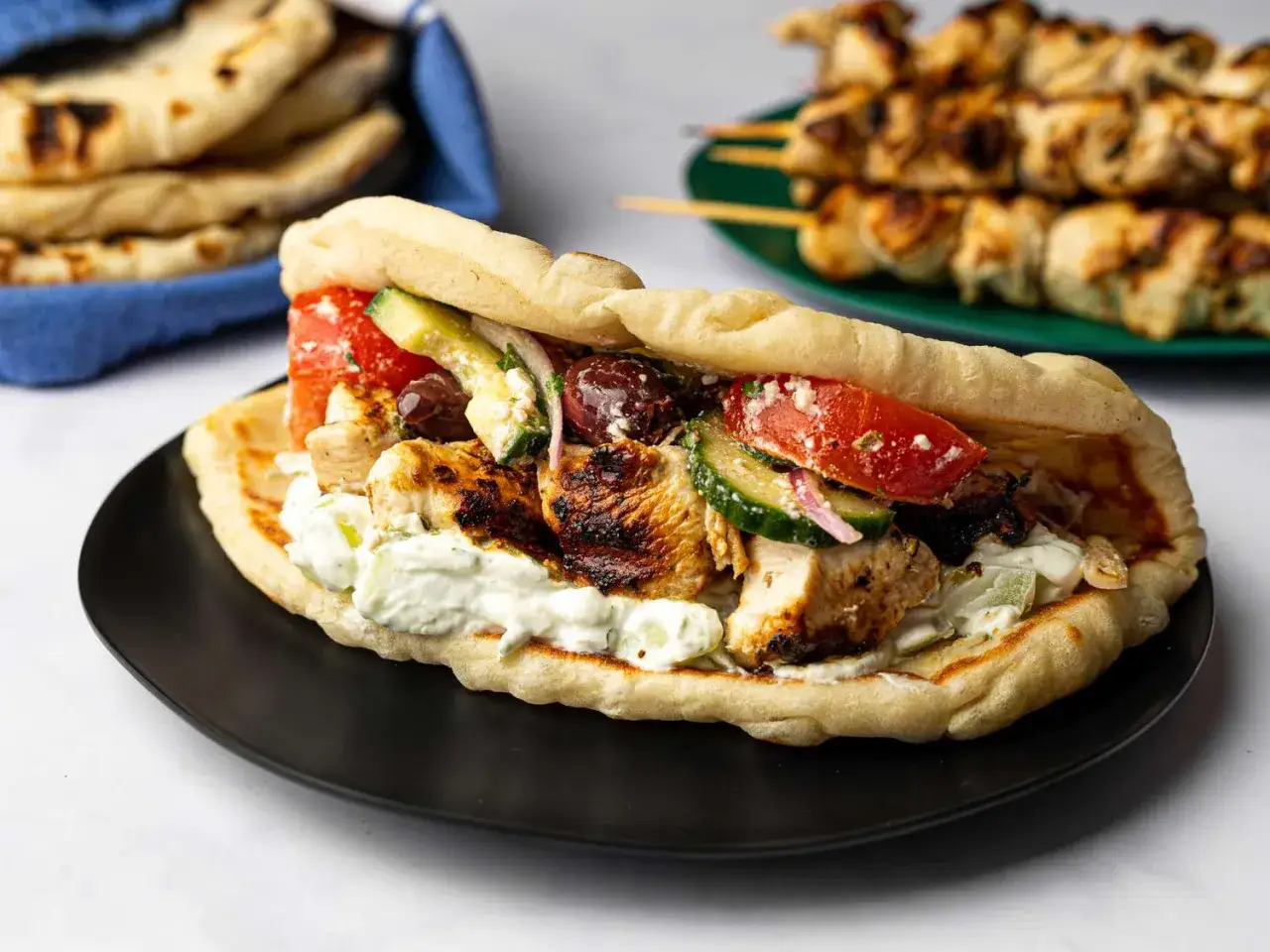 Pyszne souvlaki w picie z kurczakiem, warzywami i kremowym sosikiem. Obok stosik chlebków pita i szaszłyki.