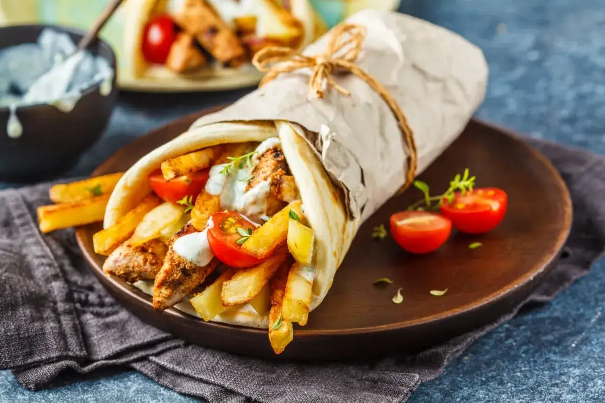 Pyszny souvlaki gyros z kurczakiem, frytkami i pomidorkami, zawinięty w papier i przewiązany sznurkiem.