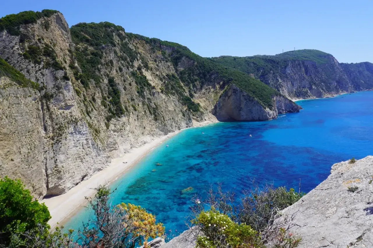 Korfu pogoda kwiecień: słoneczny dzień nad turkusowym morzem, biała plaża otoczona stromymi klifami i zielenią.