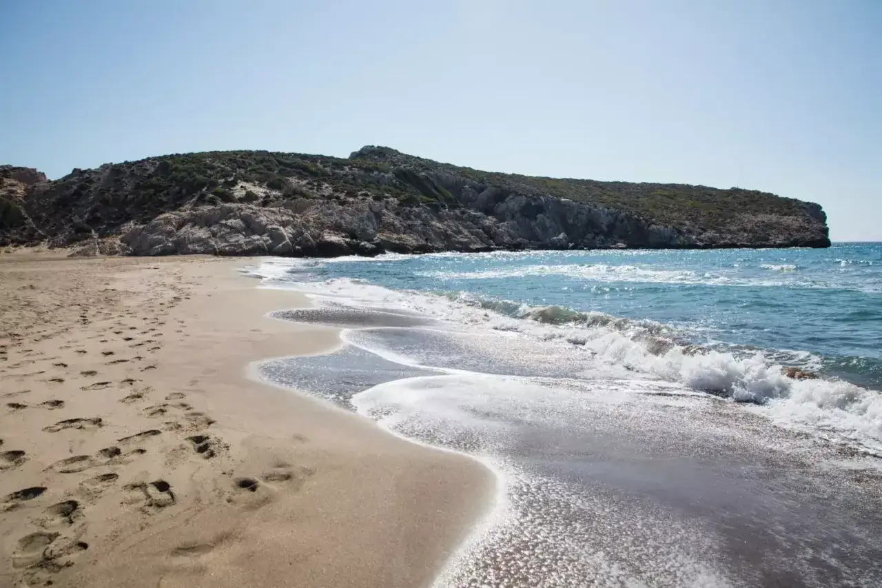 Plaża z kamienistym wzgórzem w tle i turkusowym morzem.
