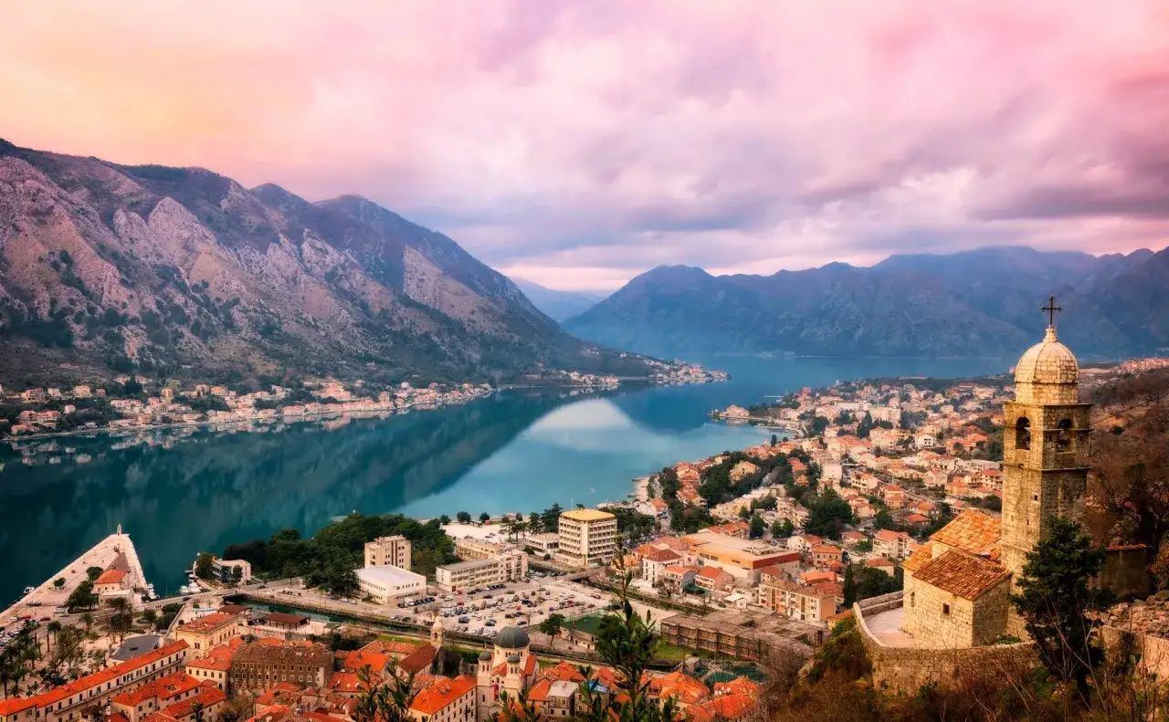 Widok na zatokę i miasto Kotor w Czarnogórze o zachodzie słońca. Góry odbijają się w spokojnej wodzie.