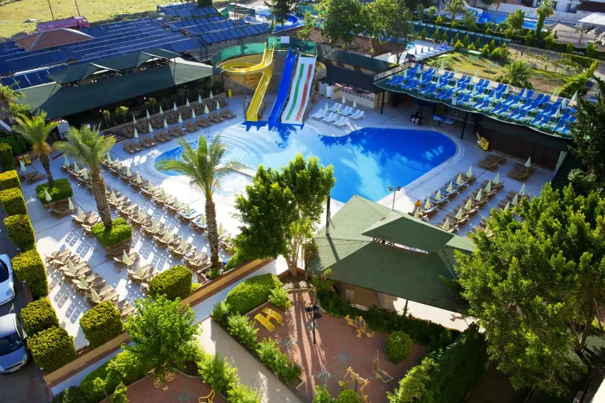 Wodne zjeżdżalnie i basen w beach club Doganay. Leżaki i palmy tworzą wakacyjny klimat.