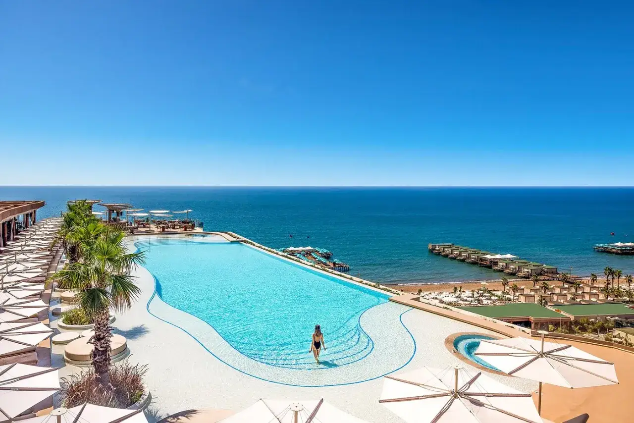 Kobieta wchodzi do basenu infinity z widokiem na morze. Luksusowy hotel oferuje wakacje ultra all inclusive.