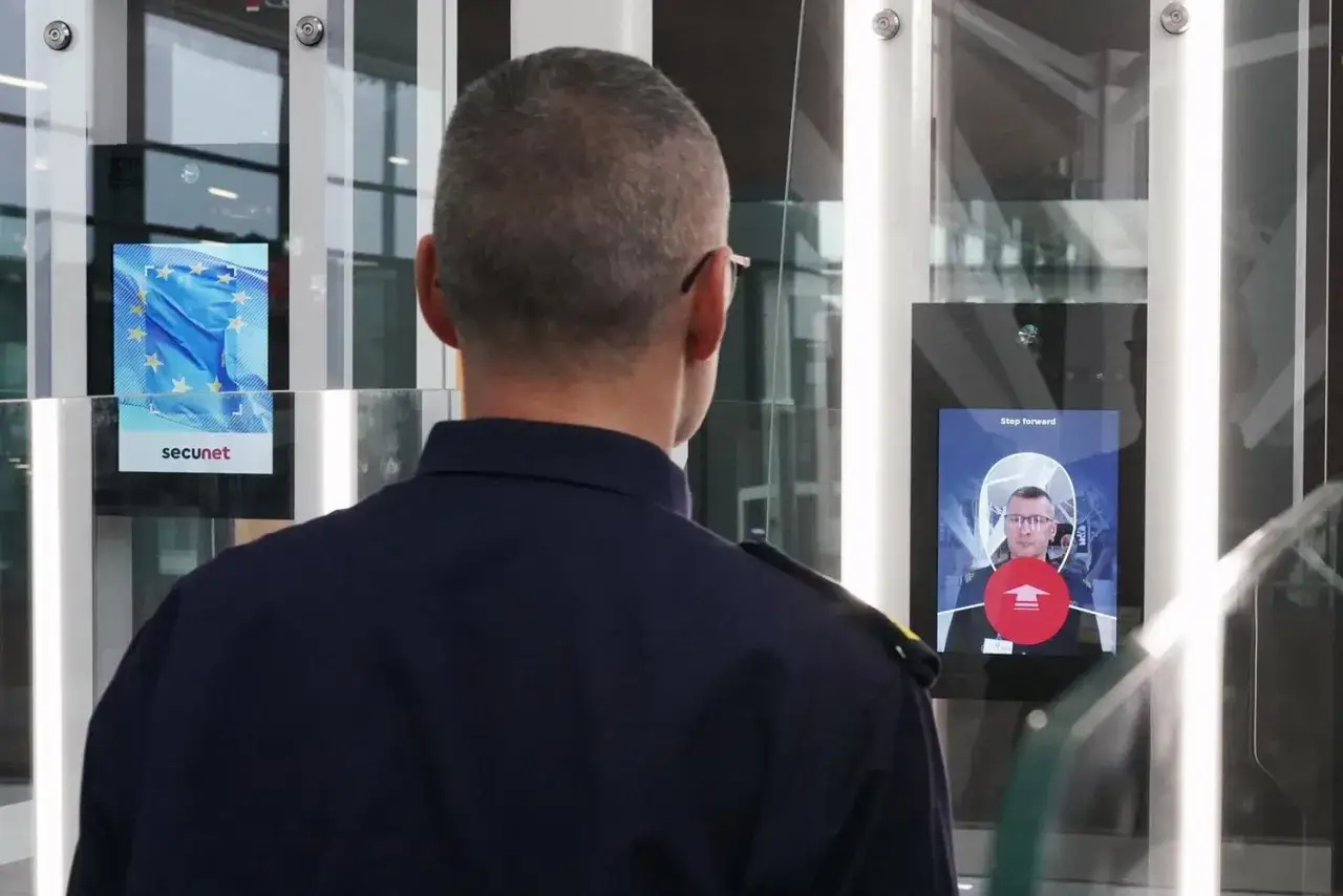 Pracownik lotniska obserwuje proces weryfikacji twarzy przed boardingiem. System Secunet skanuje pasażera, przygotowując go do odlotu.