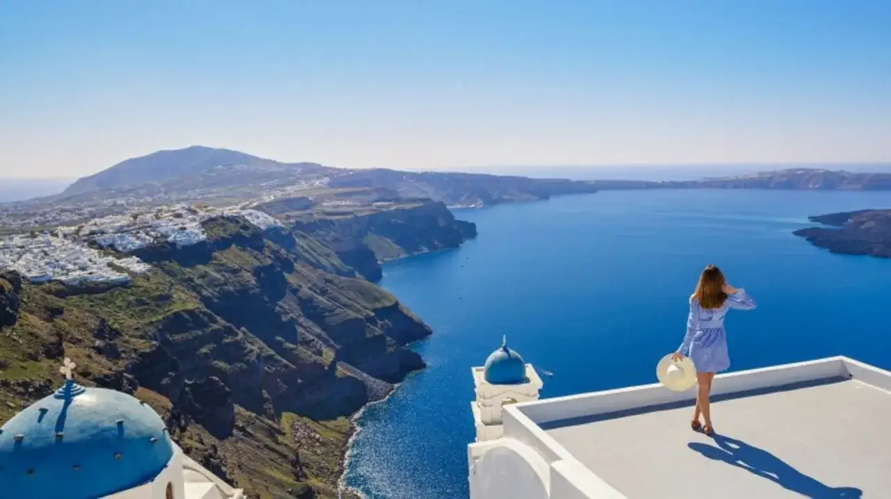 Kobieta na tarasie z widokiem na kalderę Santorini. Idealna grecja temperatura październik na wakacje.