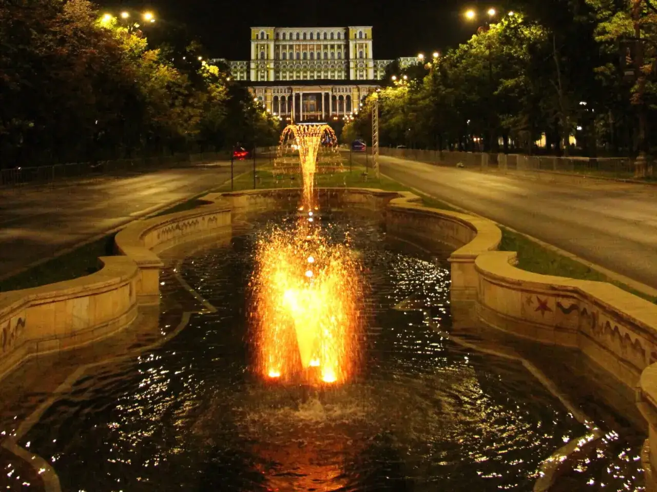 Bukareszt, nocą, fontanna rozświetla plac przed monumentalnym budynkiem.