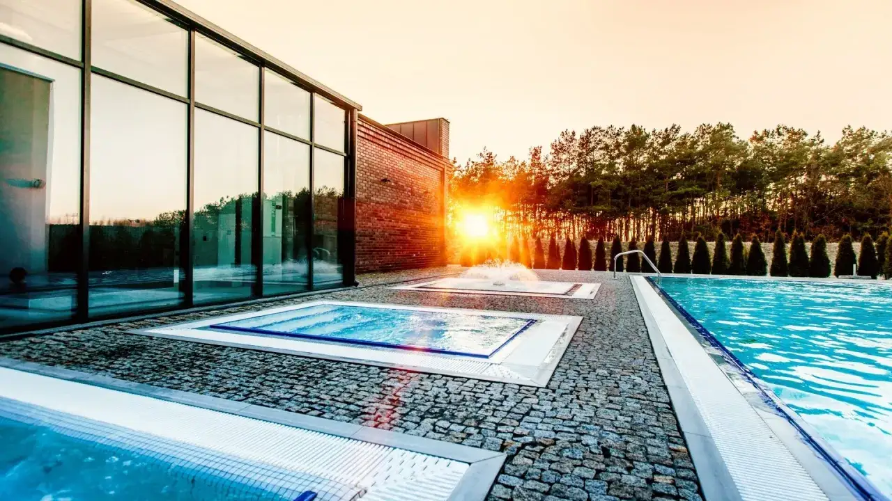 Nowoczesny hotel z basenami termalnymi, gdzie słońce zachodzi wśród drzew, tworząc magiczną atmosferę.