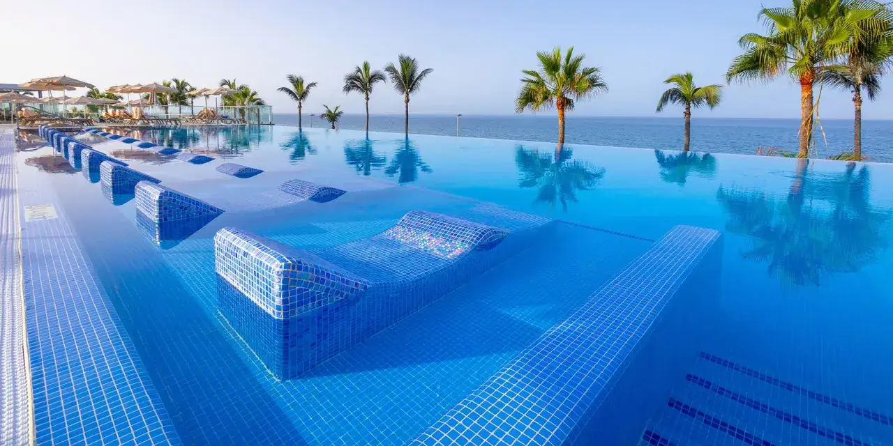 Basen infinity z leżakami w wodzie i palmami w tle. Idealne miejsce na wakacje all inclusive na Gran Canarii.