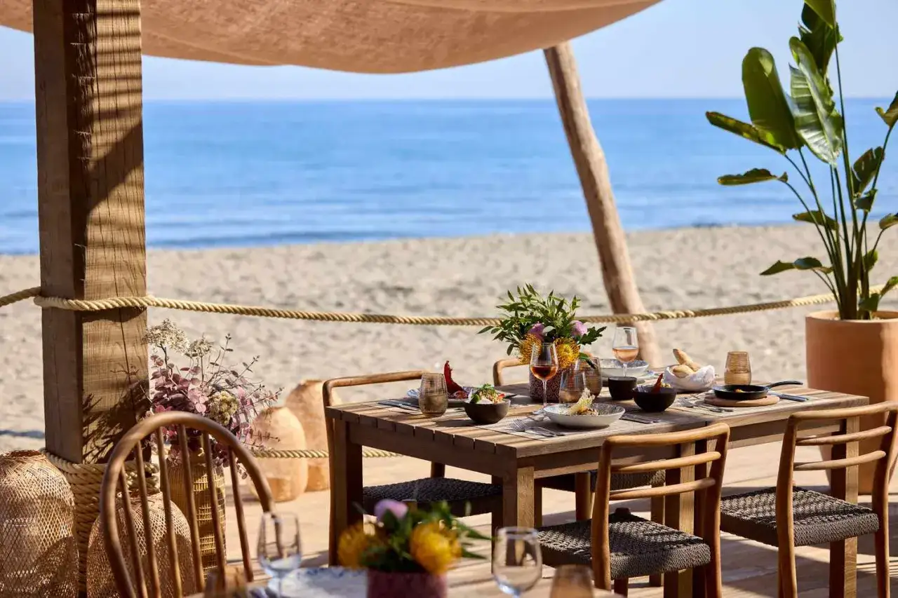 Elegancka restauracja a la carte all inclusive na plaży. Drewniany stół z jedzeniem i winem, widok na morze.