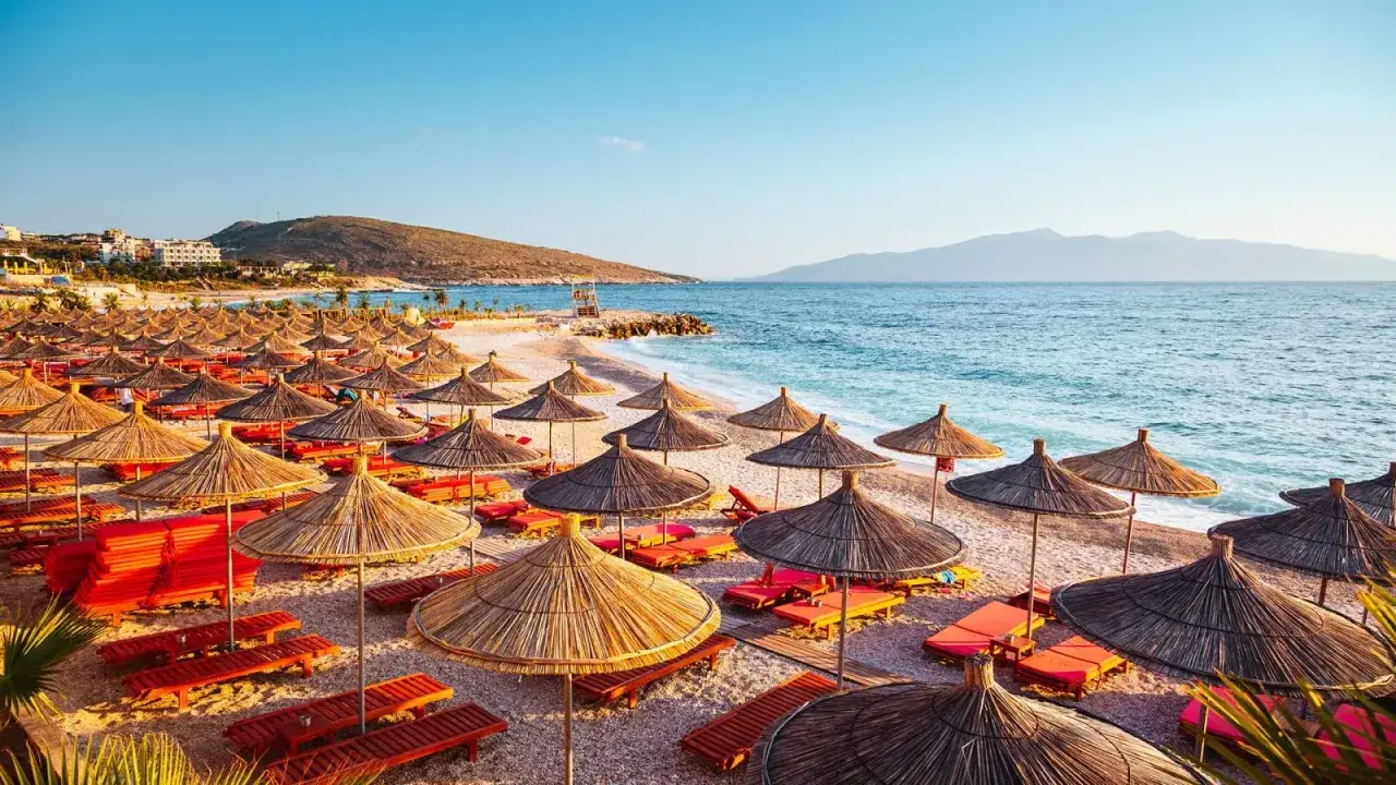 Albania pogoda październik: pusta plaża z leżakami i parasolami, morze i góry w tle.