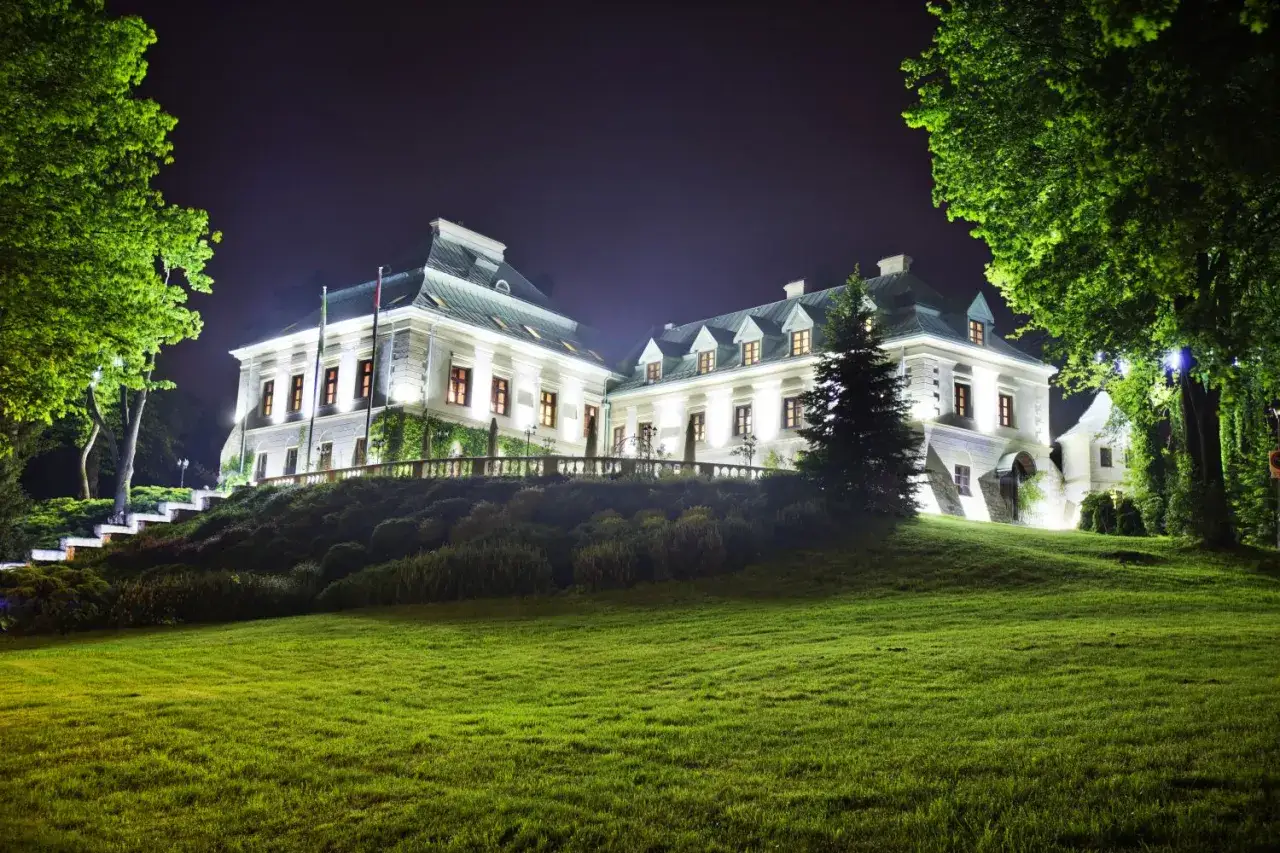 Elegancki hotel dla dorosłych, oświetlony nocą, z pięknym ogrodem i trawnikiem.