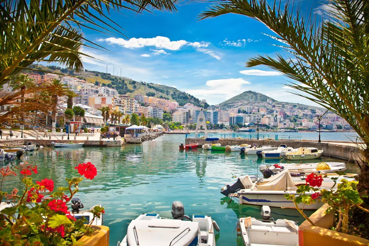 Albania, styczeń: słoneczna pogoda nad zatoką z łodziami i palmami.