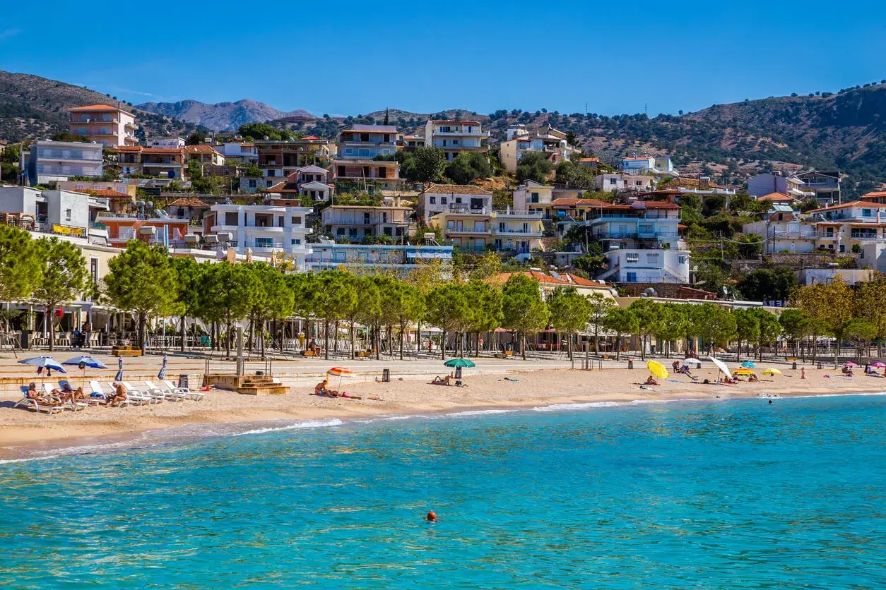 Piękna albania pogoda na plaży, z turystami relaksującymi się pod parasolami i domami na wzgórzu.