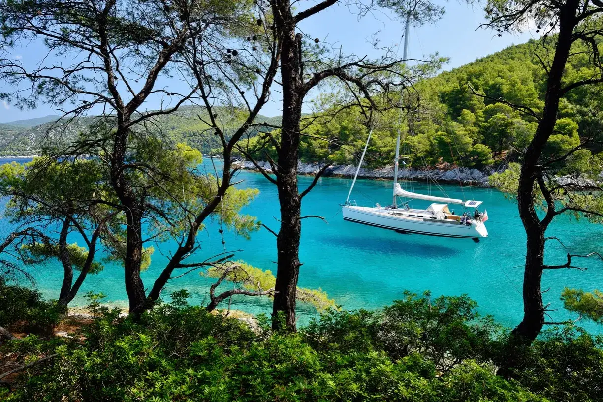 Błękitna zatoka na wyspie Skopelos, gdzie biały jacht kołysze się na turkusowej wodzie, otoczony zielenią drzew.