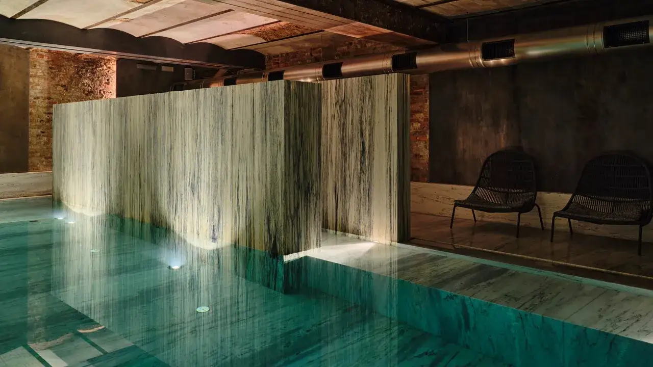 Woda w basenie luksusowego spa odbija światło, tworząc magiczną atmosferę. Dwie wiklinowe fotele czekają na gości.