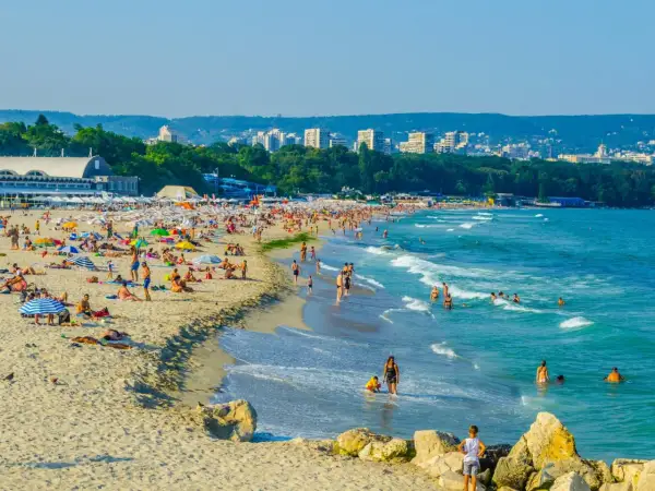 Słoneczna plaża w Bułgarii, idealna na wakacje last minute all inclusive. Tłumy ludzi opalają się i kąpią w morzu.