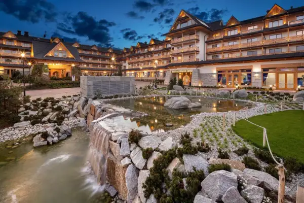 Elegancki hotel z basenami termalnymi, z kaskadą wodną i stawem w otoczeniu kamieni i zieleni.