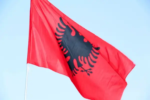 Czerwona flaga Albanii z czarnym dwugłowym orłem powiewa na tle błękitnego nieba. Zastanawiasz się, ile trwa lot do Albanii?