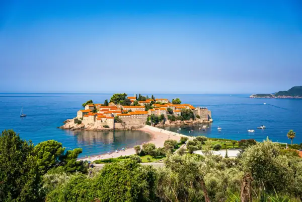 Wyspa Sveti Stefan, jedna z głównych atrakcji Budvy, otoczona turkusowym morzem, z piaszczystą plażą i łodziami.