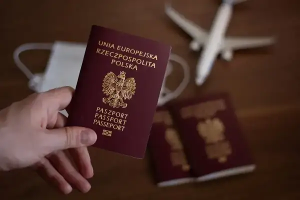 Dłoń trzyma polski paszport. Obok leżą kolejne dokumenty, maseczka i samolot. Zastanawiasz się, ile trwa wyrobienie paszportu?