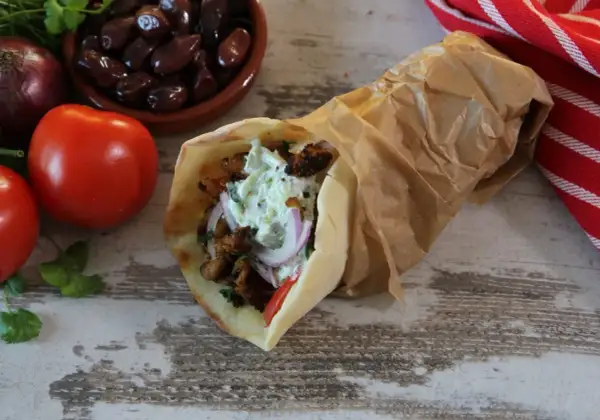 Pyszny pita gyros z mięsem, warzywami i sosem, obok pomidory, oliwki i cebula.