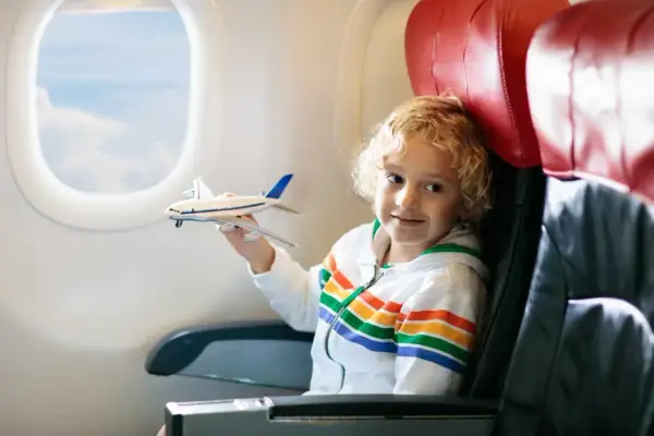 Chłopiec z blond kręconymi włosami bawi się modelem samolotu w trakcie latania samolotem.
